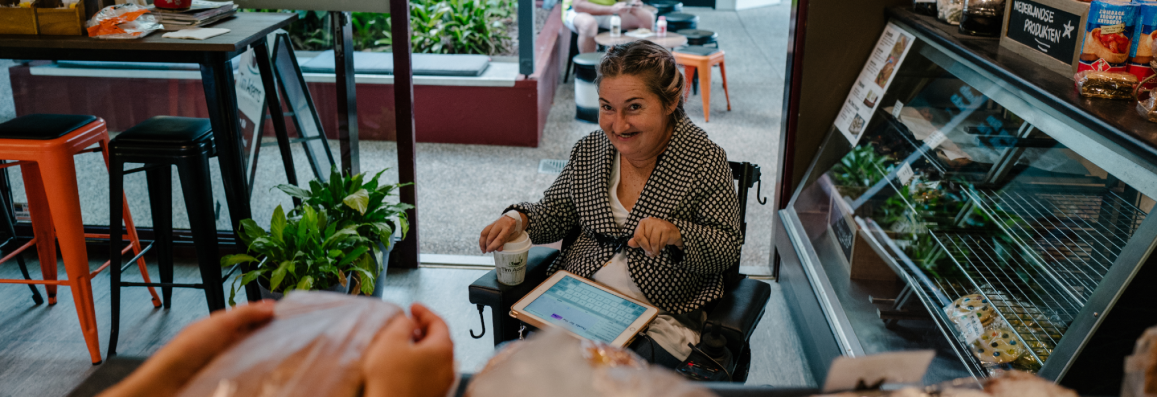 Una mujer en silla de ruedas sentada en una cafetería con un iPad usando Proloquo4Text