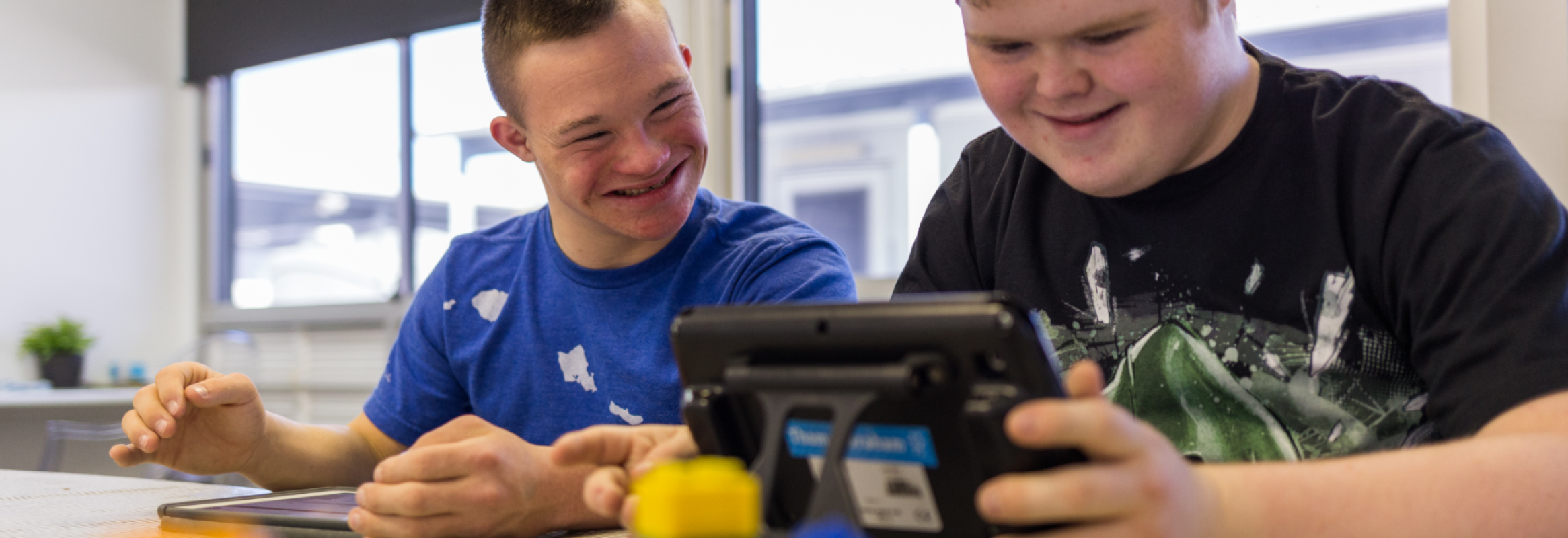 Two teenage boys sit together looking at an iPad smiling