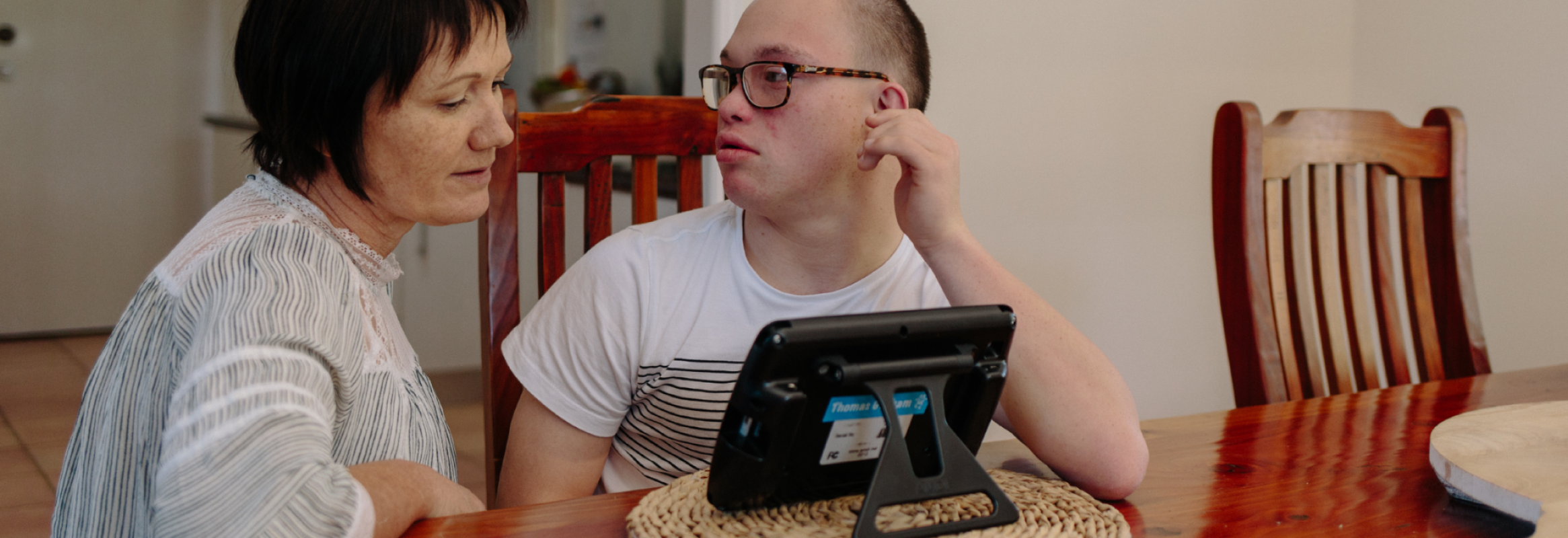 Mother and son sit together at a table around an iPad.